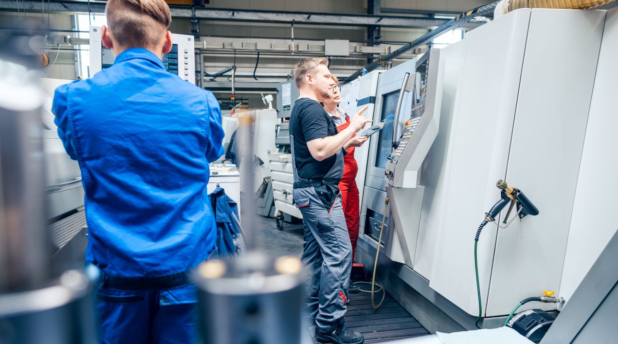 Mitarbeiter in Fertigungshalle bedienen CNC-Steuerung gemeinsam im Sondermaschinenbau zur Optimierung technischer Prozesse